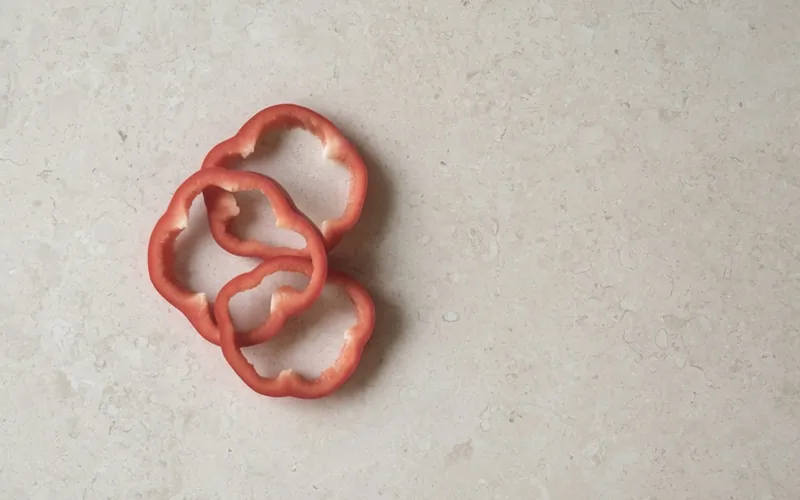 Trois rondelles de poivron rouge posées à plat sur une pierre claire, vues du dessus